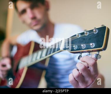 Riproduzione in sintonia. Scatto di un bel giovane che suona la chitarra a casa. Foto Stock