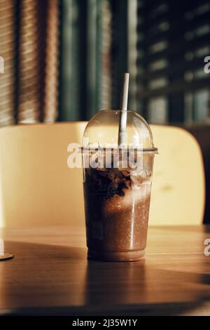 Un primo piano di frullato al cioccolato su un tavolo di legno in una caffetteria con sfondo sfocato Foto Stock