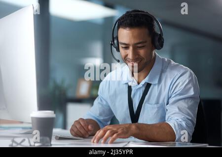 Se hai bisogno di altro, im tuo ragazzo. Scatto di un giovane che usa un auricolare e un computer in un ufficio moderno. Foto Stock