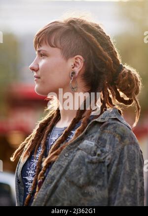 In cima alle ultime tendenze. Scatto di una giovane donna con i dreadlock e piercing in posa all'aperto. Foto Stock