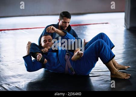 Portarlo sul tappetino. Sparo a tutta lunghezza di due giovani atleti maschi che sparano sul pavimento del loro dojo. Foto Stock