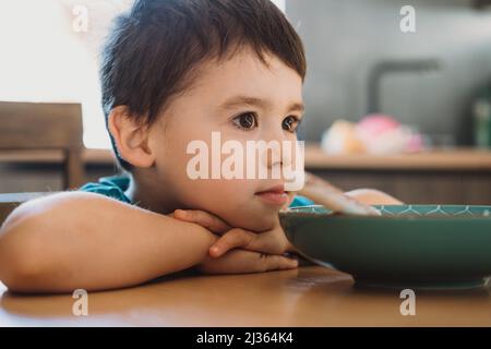 Ragazzo poggiando la testa al tavolo dopo aver mangiato bene prima di andare a scuola. Stile di vita sano. Weekend in famiglia. Foto Stock