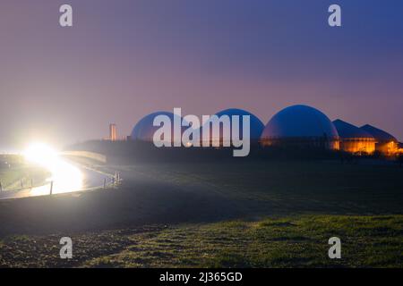 06 aprile 2022, Sassonia-Anhalt, Hohe Börde: Una giornata buia si svela su una pianta di biogas. Accanto, i primi pendolari percorrono una strada di campagna. Si suppone che rimanga nuvoloso e piovoso nella regione. Si suppone inoltre che diventi nuovamente più stormier. Un cambiamento del tempo non è in vista. Foto: Klaus-Dietmar Gabbert/dpa/ZB Foto Stock