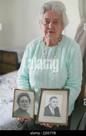 Sarà sempre ricordato. Ritratto di una donna anziana con vecchie foto in bianco e nero di un uomo e di una donna. Foto Stock