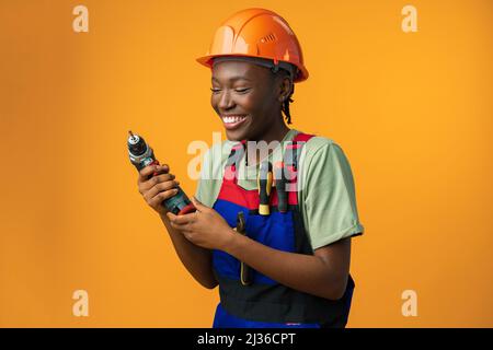 Sorridente giovane afroamericana in hardhat tenendo utensile cacciavite in studio Foto Stock