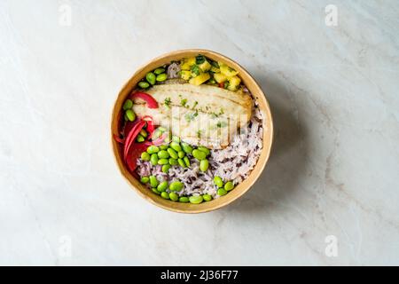 Ciotola di poke di pesce con fagioli Edamame, riso Basmati, cipolla e cubo di ananas tritato in contenitore da asporto in plastica Foto Stock