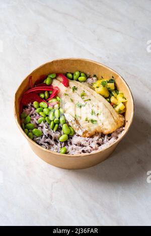 Ciotola di poke di pesce con fagioli Edamame, riso Basmati, cipolla e cubo di ananas tritato in contenitore da asporto in plastica Foto Stock