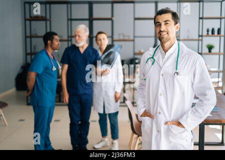 Ritratto di sorridente medico maschile indossando uniforme bianca in piedi in ufficio medico riunione, guardando la macchina fotografica. Foto Stock