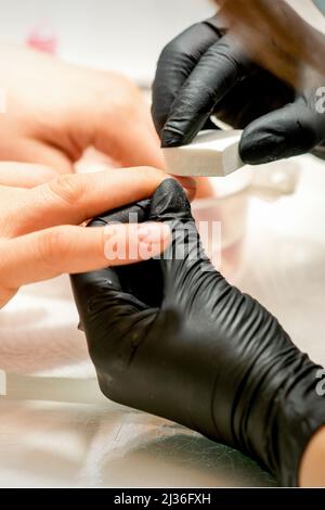 Primo piano delle mani caucasiche di un manicurista professionale stanno archiviando le unghie di una giovane donna. Giovane donna caucasica che riceve una manicure da un estetista con una lima del chiodo in un salone del chiodo Foto Stock