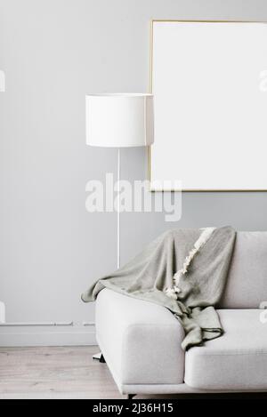 Interni eleganti e minimalisti del soggiorno in grigio. Divano con plaid, piantana e montatura bianca mockup a parete Foto Stock