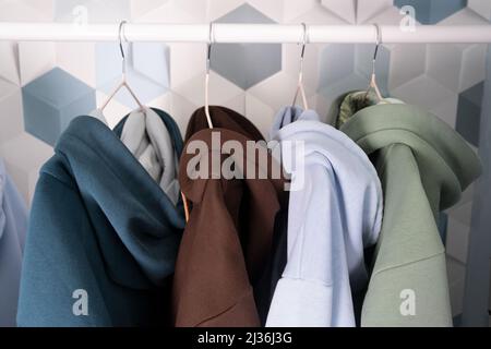 Fila di felpe con cappuccio multicolore in maglia, maglioni sportivi appesi su un appendino in un atelier o abbigliamento sportivo del negozio Retail in primo piano. Colori pastello freddi. Foto Stock