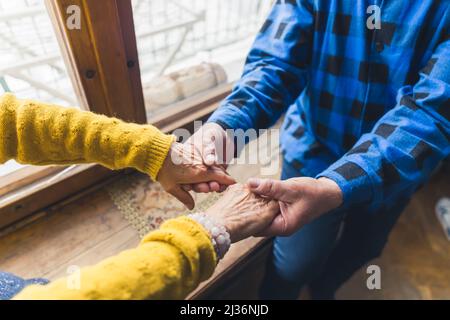 Anziano anziano coppia sposata che tiene le loro mani rugose contro la finestra durante l'inverno Close up Amore in età avanzata. Foto di alta qualità Foto Stock