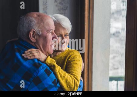 Anziani anziani sposati coppia abbracciando e abbracciando accanto alla finestra durante l'inverno - l'amore e la convivenza in giovane età . Foto di alta qualità Foto Stock