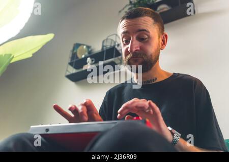 Buon uomo europeo giovane che suona su un piccolo sintetizzatore di suono moderno in studio medio primo piano stanza interna sfondo . Foto di alta qualità Foto Stock