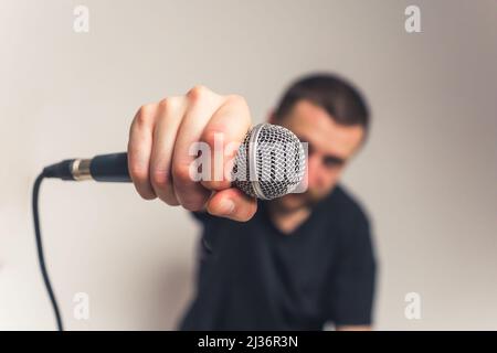 Giovane europeo dall'aspetto bello con tatuaggi baffi e microfono che guarda nello studio medio closeup della fotocamera, ha scattato uno sfondo chiaro. Foto di alta qualità Foto Stock