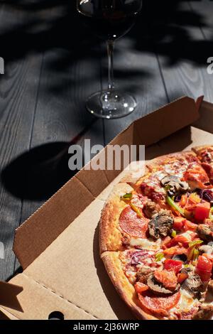 Una scatola di pizza e un bicchiere di vino in una giornata estiva. Concetto di consegna pizza. Foto verticale. Foto Stock