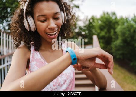 Giovane donna nera con cuffie che utilizzano lo smartwatch mentre si allenano all'aperto Foto Stock