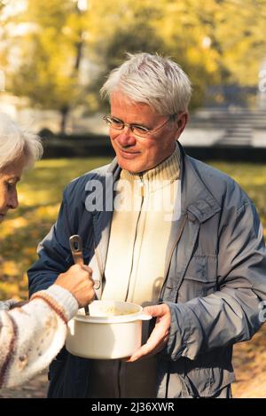 Uomo caucasico invecchiato in occhiali e abbigliamento casual ottenere o offrire cibo a una donna natura sfondo persone anziane benessere sostegno concetto medio shot fuoco selettivo . Foto di alta qualità Foto Stock