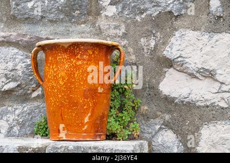 Vaso in ceramica arancione antico si erge contro un muro di pietra. Foto Stock