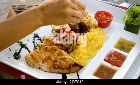 Lo chef spremere a mano il succo di limone al piatto di pesce con gamberi alla griglia al carbone Foto Stock