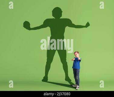 Immagine concettuale con ragazzino che sogna la futura carriera sportiva e l'ombra del calciatore americano maschile su sfondo verde. Foto Stock