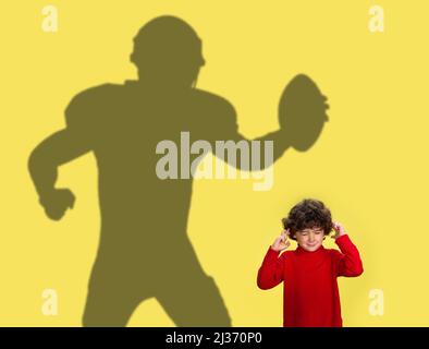 Immagine concettuale con il ragazzino che sogna la futura carriera sportiva e l'ombra del calciatore americano maschile su sfondo giallo. Foto Stock