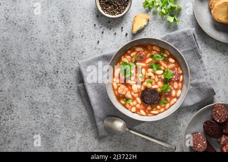 Fabada spagnola servita su sfondo grigio. Fabada fa di aricot, chorizo, malcillas o salsiccia di sangue, pomodori. Vista dall'alto. Spazio di copia. Foto Stock