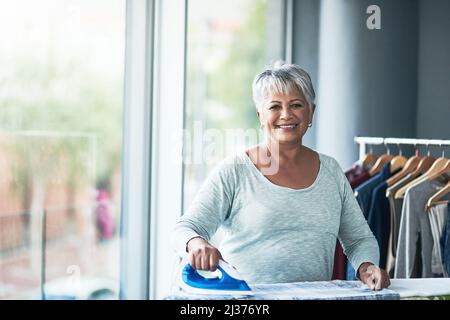 E' un piacere avere abiti appena spremuti. Ritratto di una donna matura stirando abiti a casa. Foto Stock