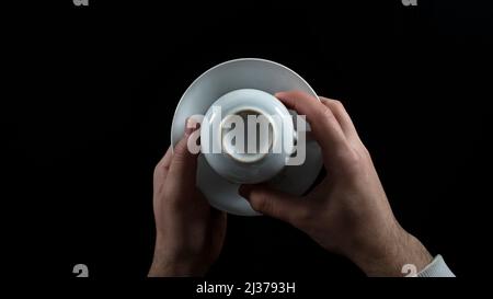 Tazza di caffè bianca rovesciata, che racconta la fortuna, mani maschili, isolata su sfondo nero, vista dall'alto Foto Stock