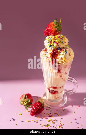 Gelato alla vaniglia, milkshake guarnito con fragole fresche e spolverini colorati su sfondo rosa Foto Stock