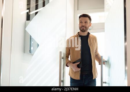 Un uomo d'affari allegro che entra nel suo ufficio aprendo la porta di vetro Foto Stock