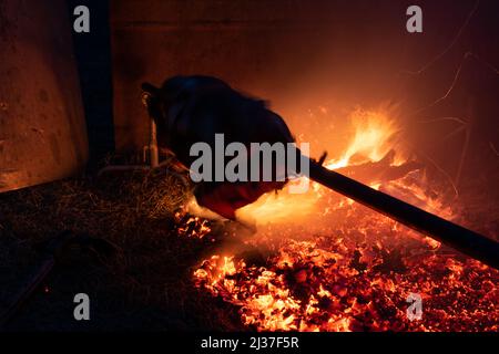 Silhouette di maiale intero che gira su una spit sopra la piastra del fuoco in calore e fumo di notte in lunga esposizione, rotisserie o spit arrostimento, ortodosso serbo Foto Stock