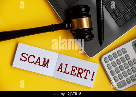 Scam testo di avviso su blocco note con gavel, laptop, penna e sfondo calcolatrice. Foto Stock