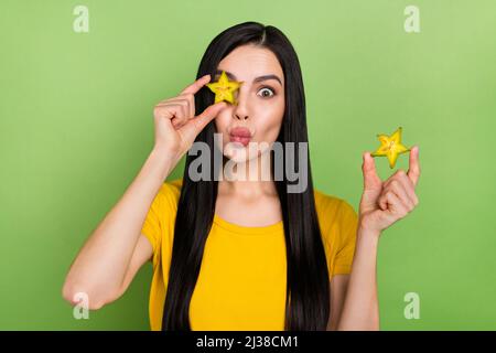 Foto di stolante impressionato donna indossare giallo t-shirt tenuta tropicale frutta copertura occhi labbra plump isolato verde sfondo di colore Foto Stock