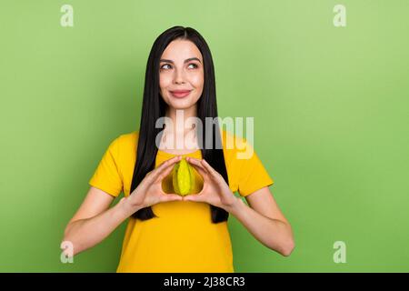 Foto di signora funky sognante vestito giallo t-shirt tenendo frutta esotica cercando spazio vuoto isolato sfondo verde colore Foto Stock