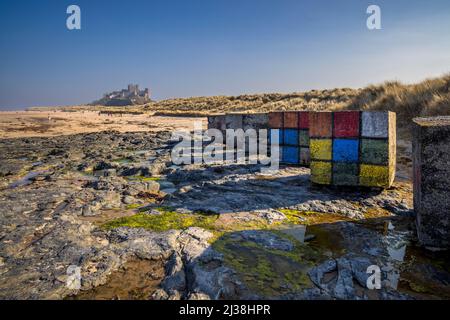 Decorato la seconda guerra mondiale cubetti di cemento anticarro sulla spiaggia di Bambburgh con il Castello di Bambburgh sullo sfondo, Northumberland, Inghilterra Foto Stock