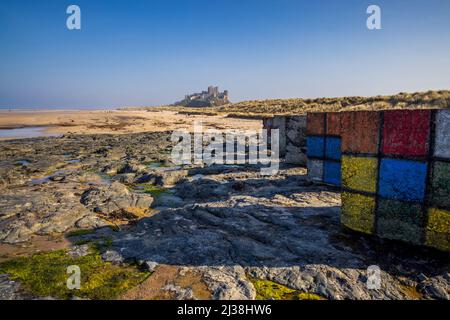 Decorato la seconda guerra mondiale cubetti di cemento anticarro sulla spiaggia di Bambburgh con il Castello di Bambburgh sullo sfondo, Northumberland, Inghilterra Foto Stock