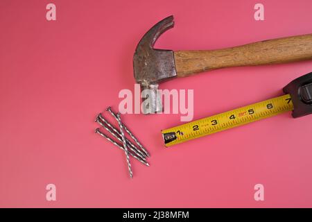 Flatlay di martello, chiodi e metro a nastro isolato su sfondo rosa Foto Stock