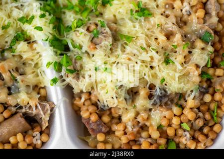 Pasta di semola rotonda con carne di maiale affettata, salsa, funghi e formaggio grattugiato e erba cipollina in scatola di plastica. Togliere il pasto, primo piano. Foto Stock