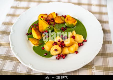 Palle di formaggio affumicato, patate fritte, salsa di spinaci e semi di melograno su piatto bianco sul tavolo. Foto Stock