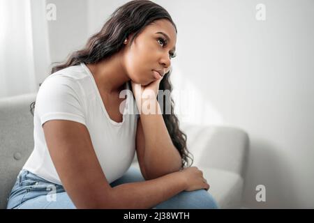 Stressata miserabile donna nera soffre di dolore problema, depressa solitario sconvolto ragazza africana piangendo da solo sul divano Foto Stock