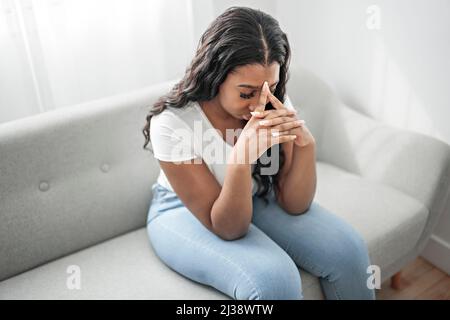 Stressata miserabile donna nera soffre di dolore problema, depressa solitario sconvolto ragazza africana piangendo da solo sul divano Foto Stock