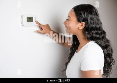 Donna africana signora che regola il pannello di controllo della climatizzazione sulla parete termostato Foto Stock