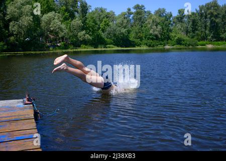 Ragazzino che salta in testa nell'acqua del fiume dal molo di legno. Kiev, Ucraina Foto Stock