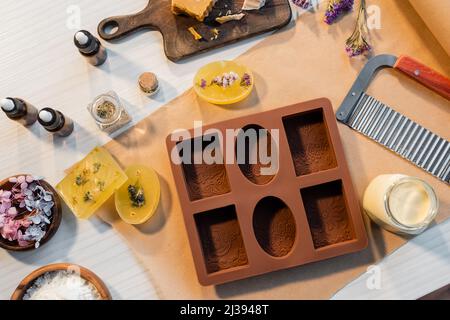 Vista dall'alto del sapone fatto a mano vicino a muffa di silicone, fiori e oli essenziali sul tavolo Foto Stock