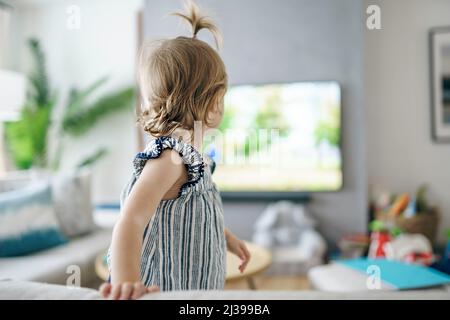 ragazza piccola carina dal retro guardando la tv a casa Foto Stock