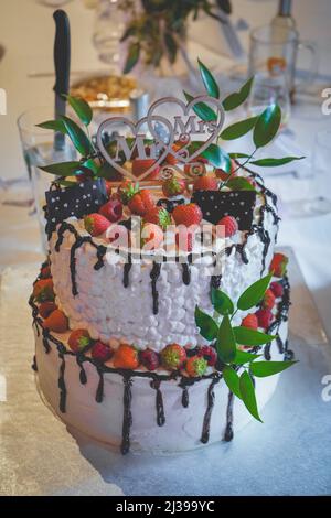 Un colpo verticale di bella e deliziosa torta nuziale coperta di panna, cioccolato e fragole Foto Stock