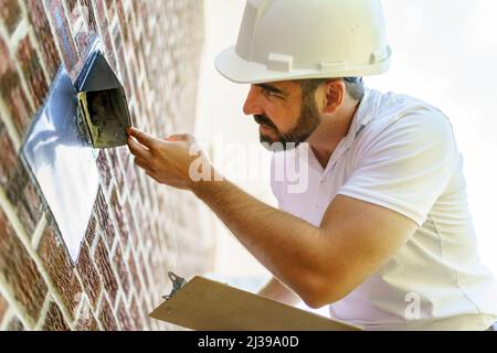 uomo con un elmetto bianco che tiene una clipboard, ispezionare casa Foto Stock