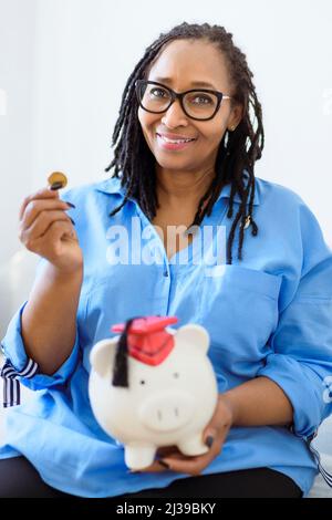 Bella donna nera tiene una banca rosa piggy che rappresenta il risparmio e la pensione Foto Stock