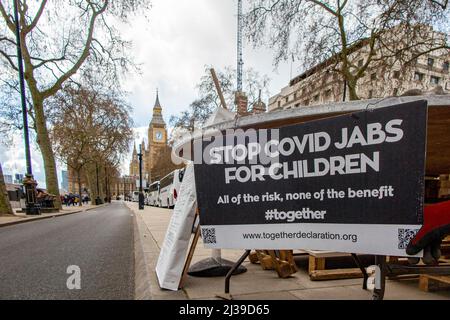 Una targhetta all'esterno della tenda di un dimostratore contro la vaccinazione dei bambini per Covid 19 con Big ben in lontananza Foto Stock